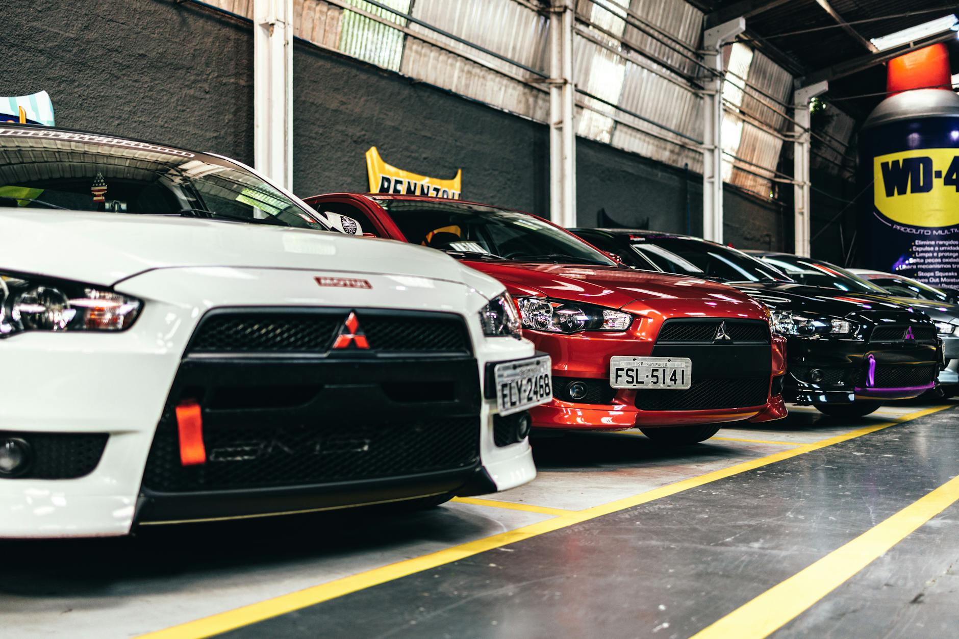 Ilustrasi: Close-up of parked Mitsubishi Lancer cars in an indoor lot featuring a variety of colors.