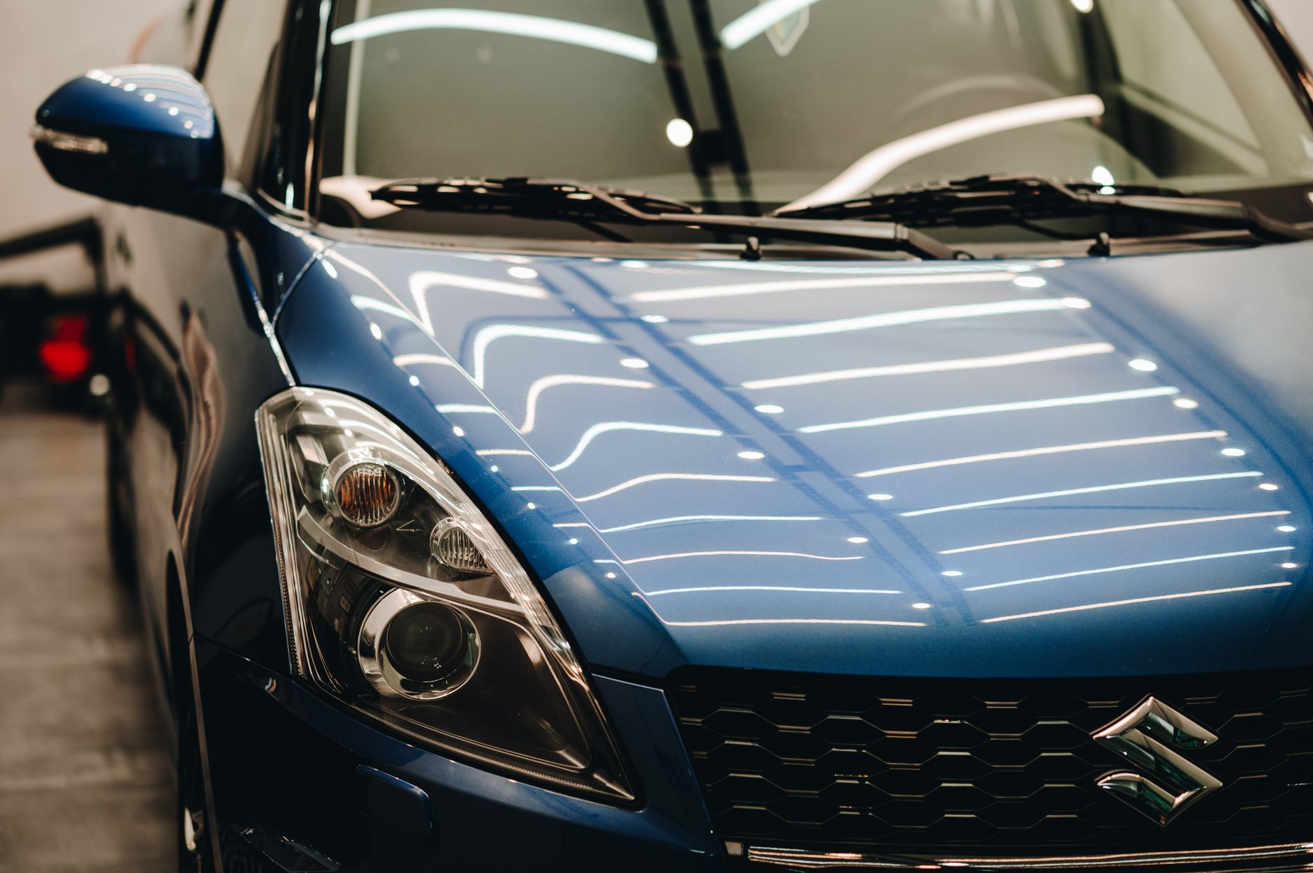 Ilustrasi: Close-up of a stylish blue Suzuki car displayed in a well-lit showroom with modern reflections.