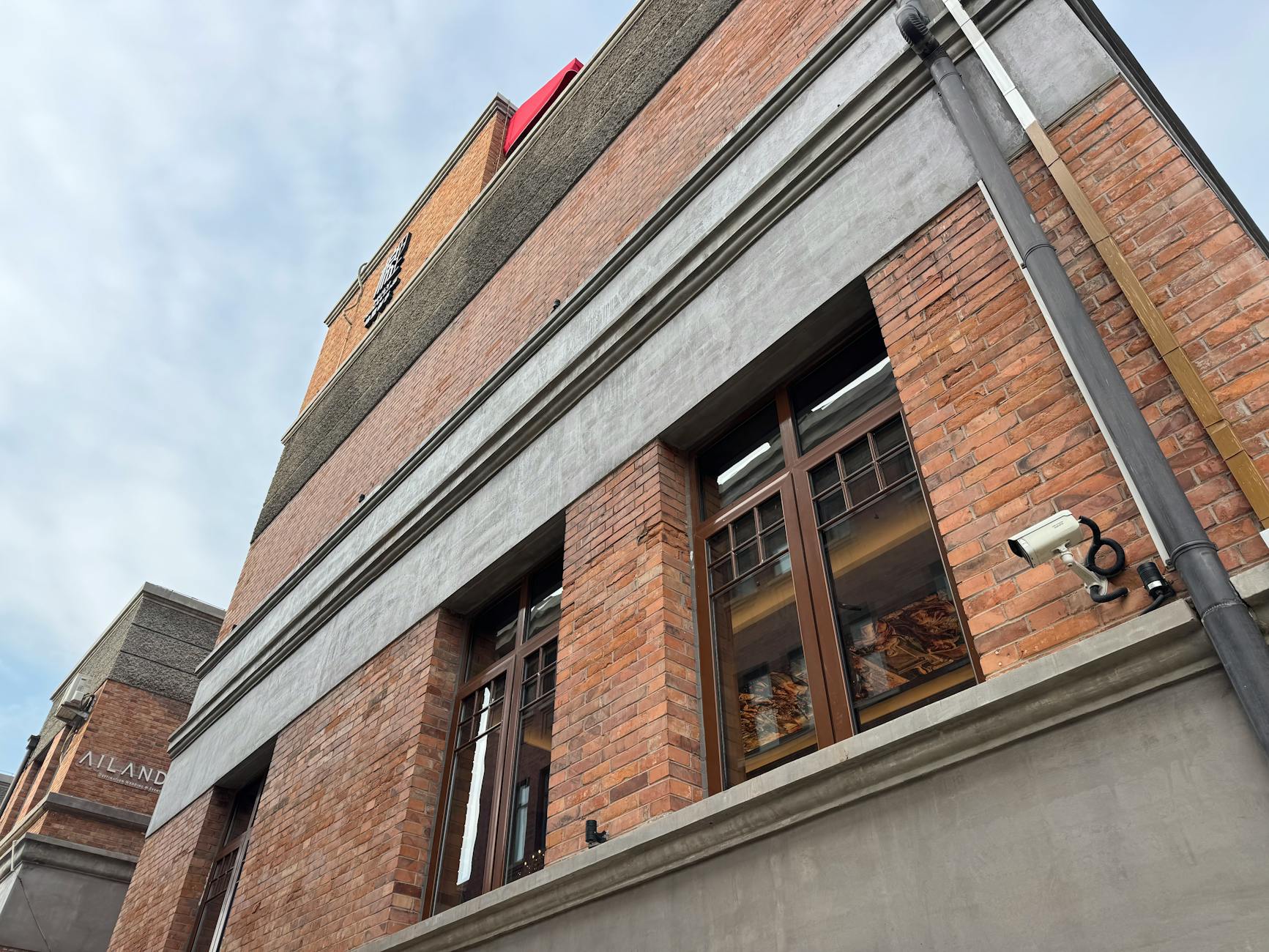 Ilustrasi: Low angle view of a red brick building facade with windows and a security camera.