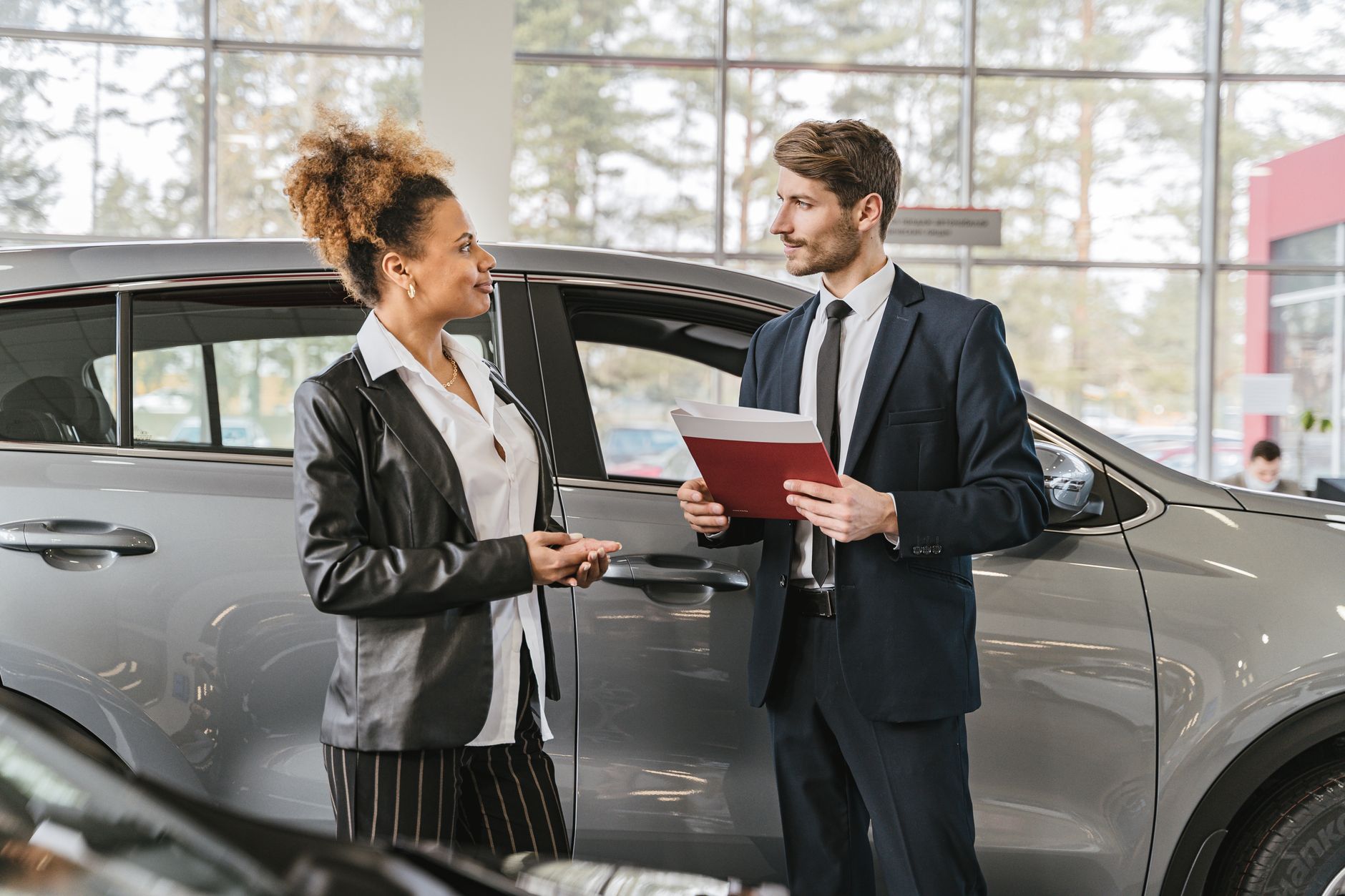 Ilustrasi: A woman discussing car purchase with a dealer inside a car dealership showroom.