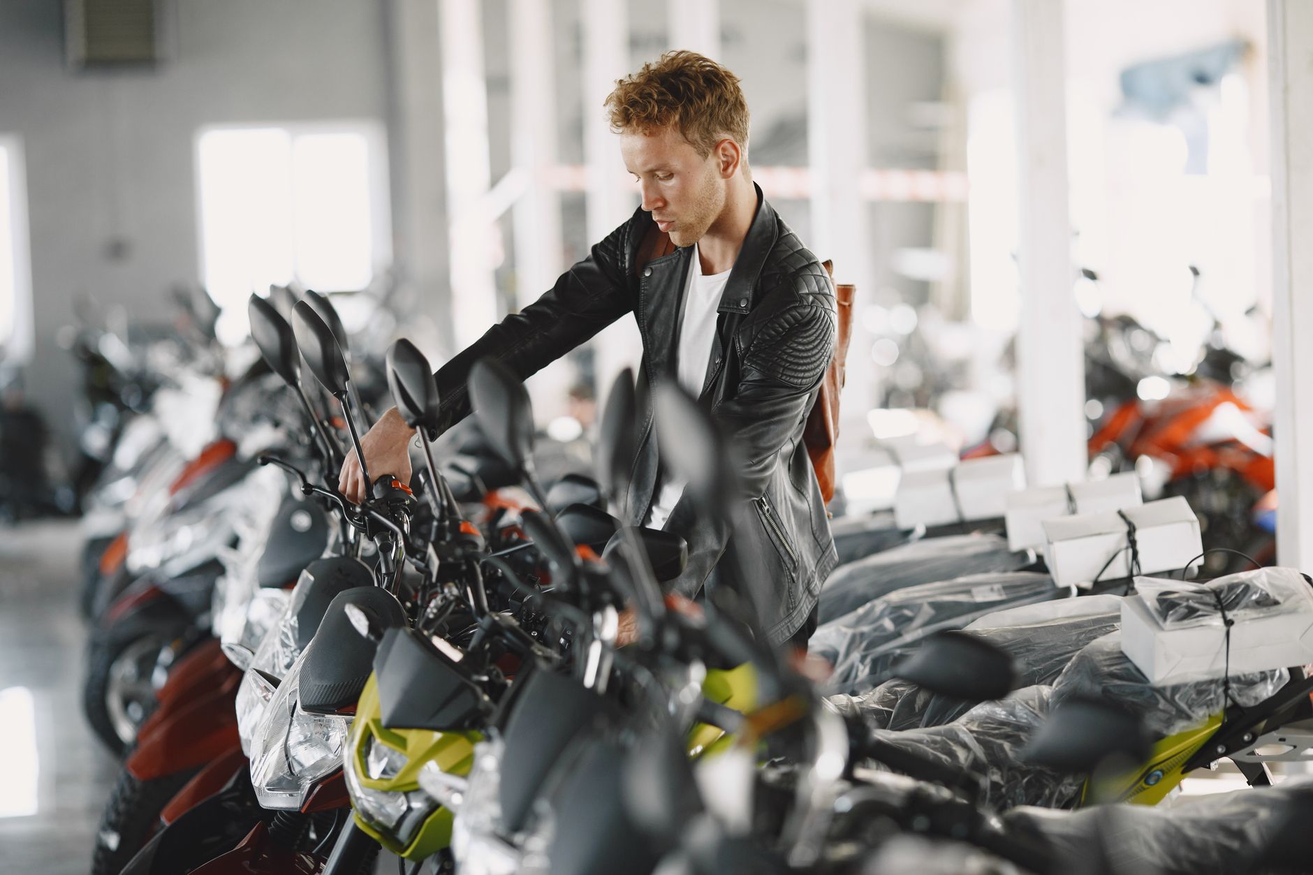Ilustrasi: Man inspecting motorcycles indoors at a dealership showroom.