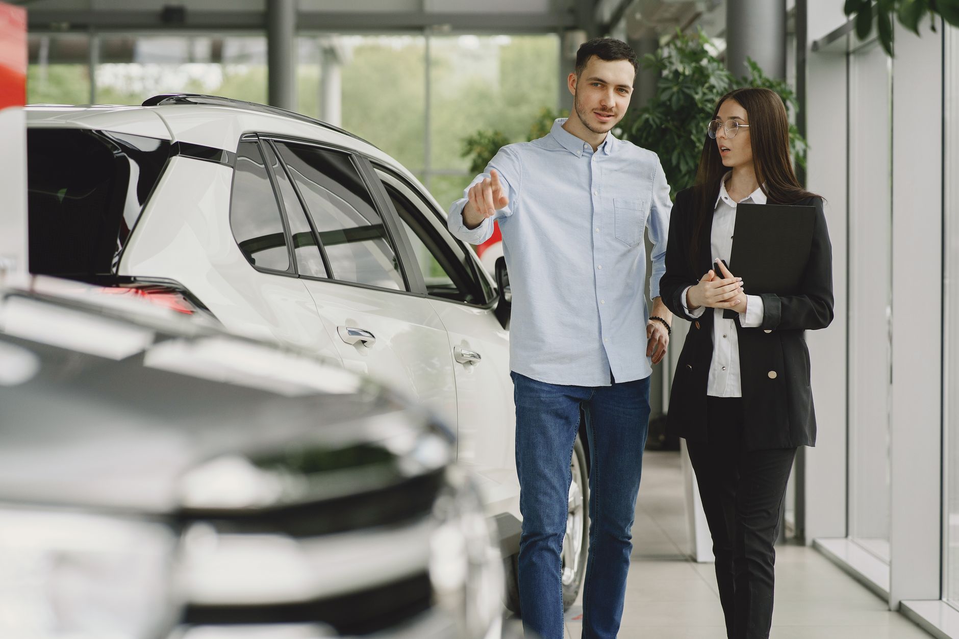 Ilustrasi: Customer and salesperson discussing a vehicle inside a modern car dealership showroom.