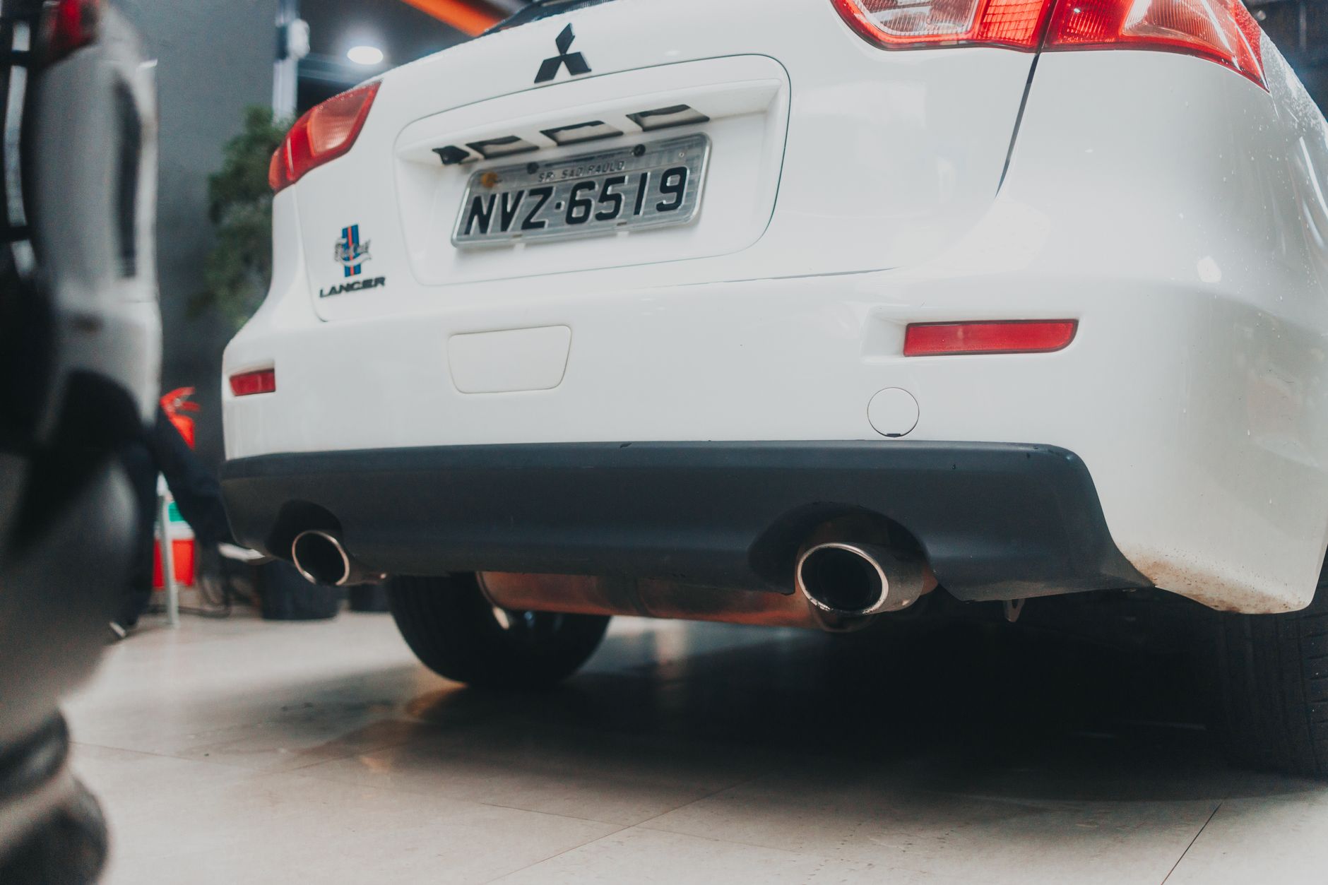Ilustrasi: Close-up of a white Mitsubishi Lancer showcasing its exhaust and rear design in an indoor setting.
