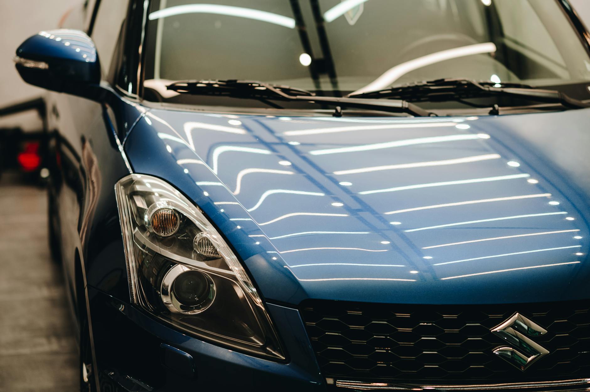 Ilustrasi: Close-up of a stylish blue Suzuki car displayed in a well-lit showroom with modern reflections.