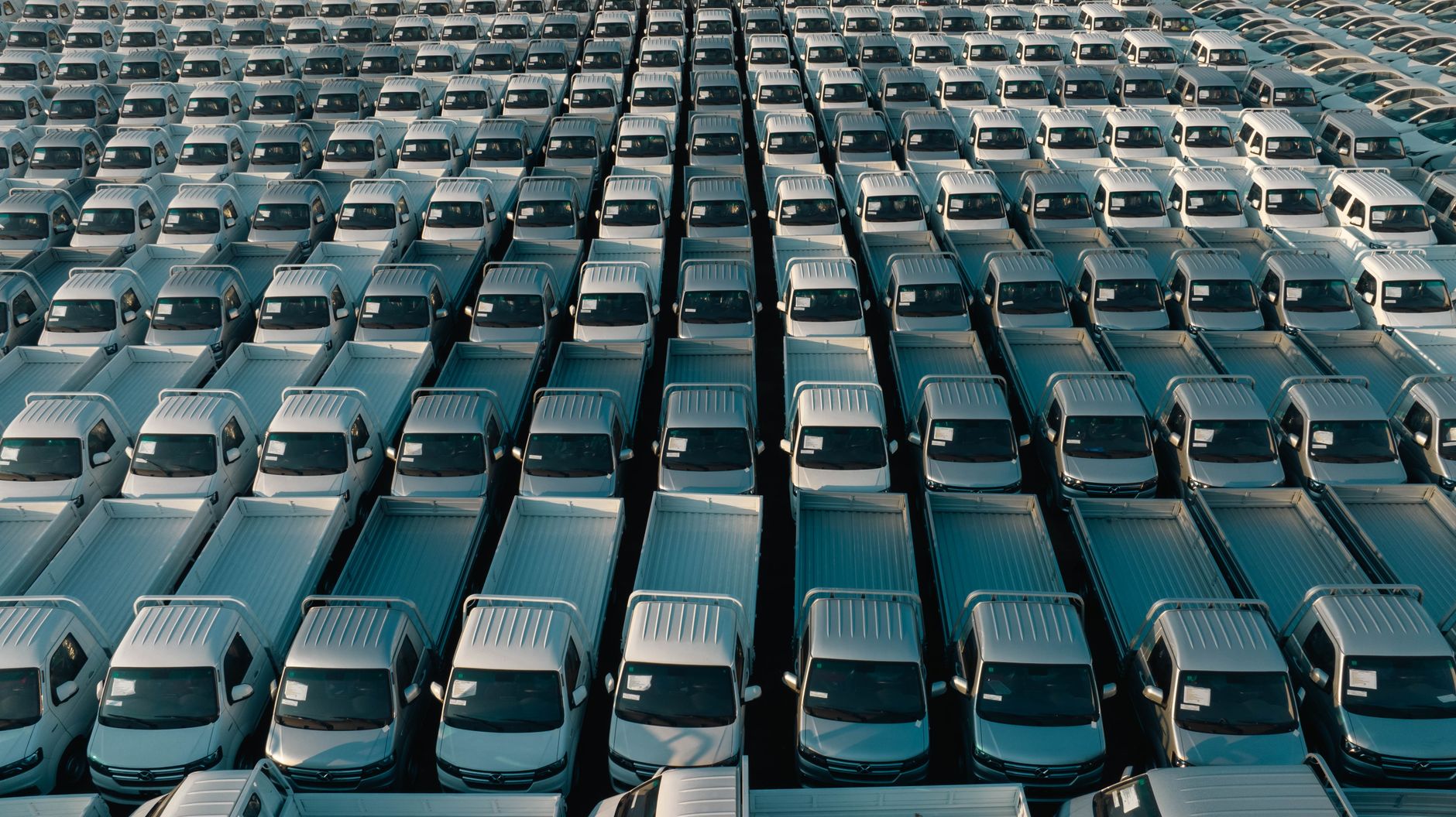 Ilustrasi: Overhead shot of a large collection of white pickup trucks parked in neat rows, emphasizing industrial scale.