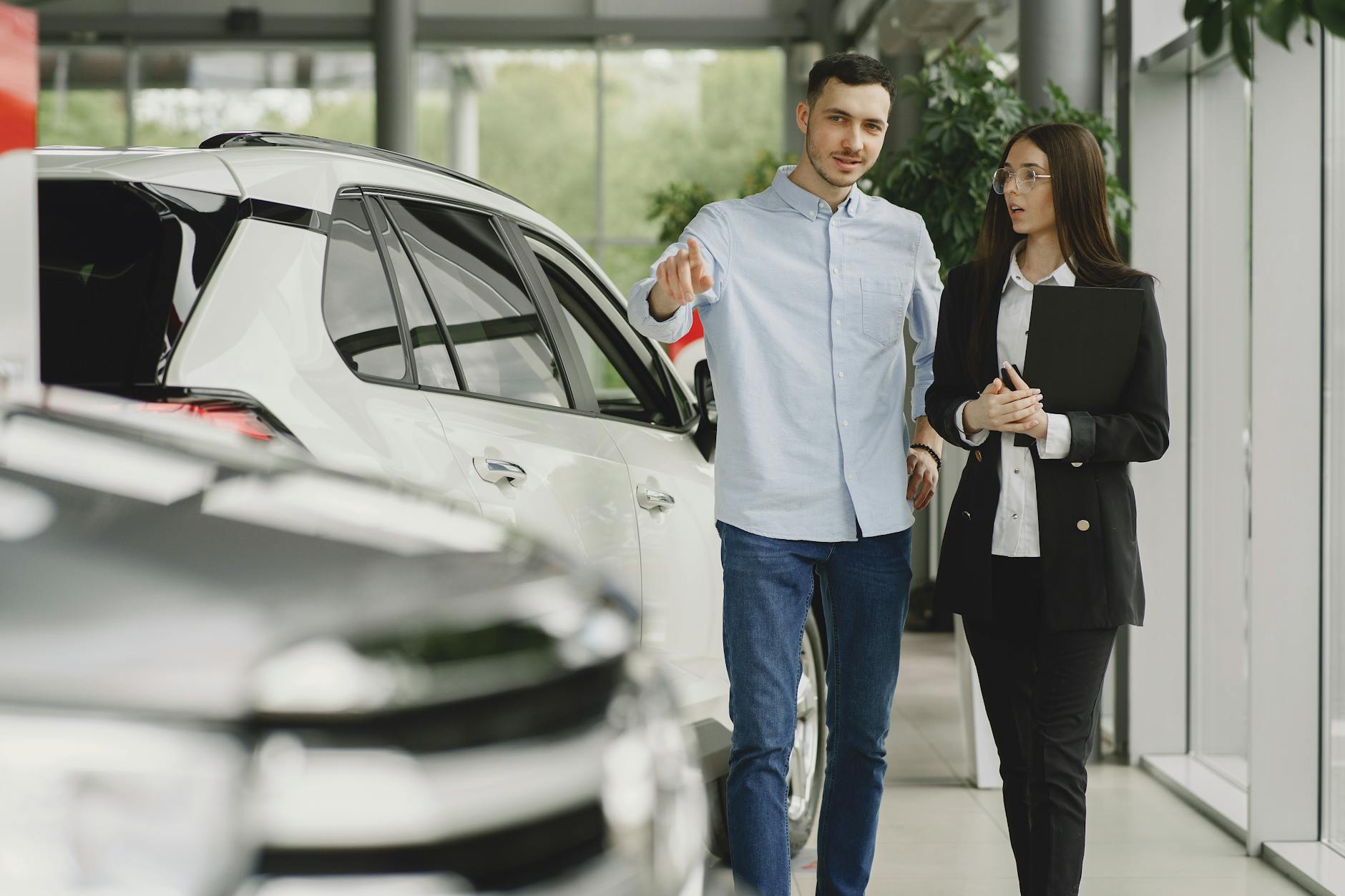 Ilustrasi: Customer and salesperson discussing a vehicle inside a modern car dealership showroom.