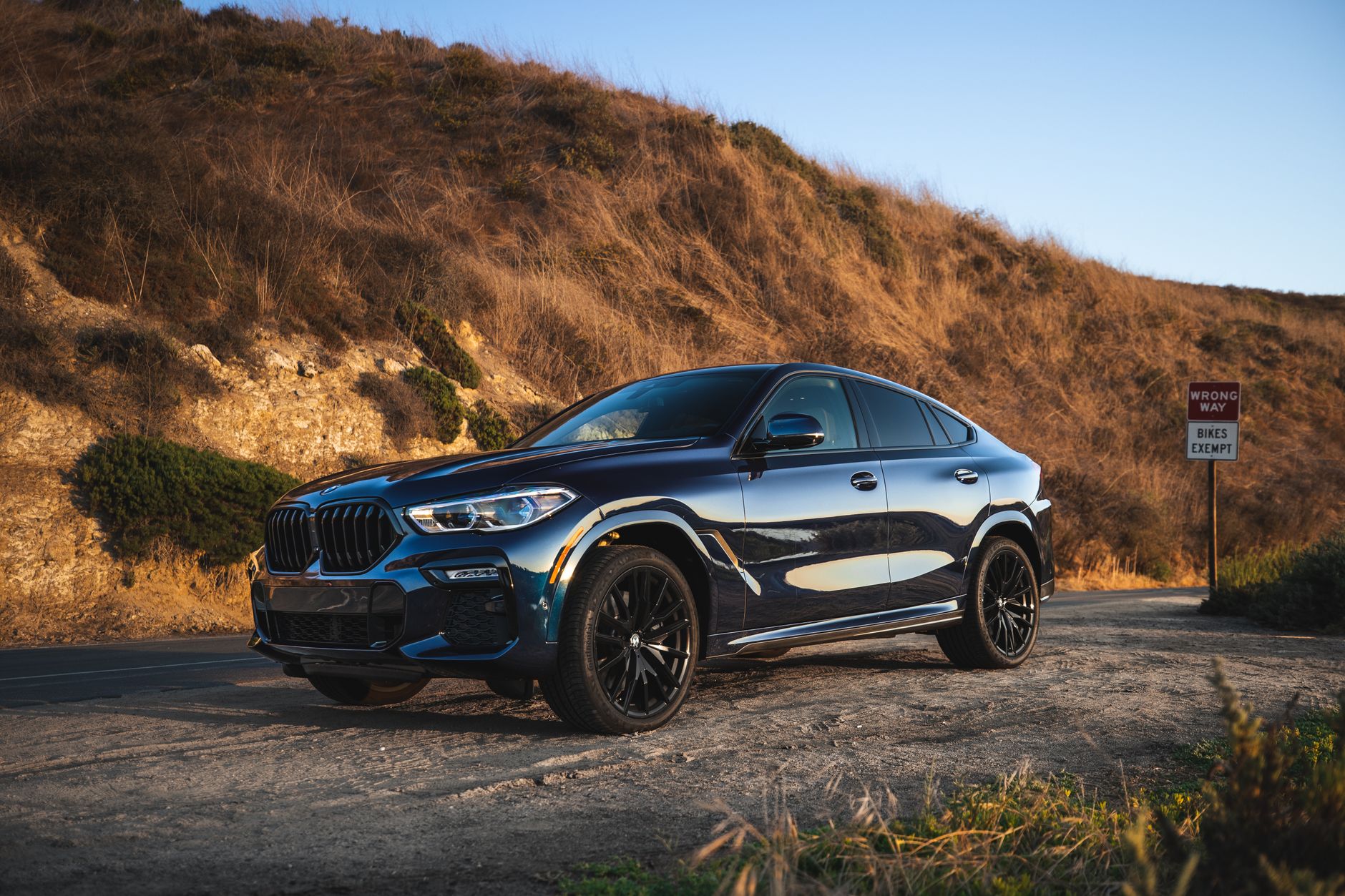 Ilustrasi: Elegant black BMW SUV parked on a scenic dirt road in Newport Beach, capturing the sunset glow.