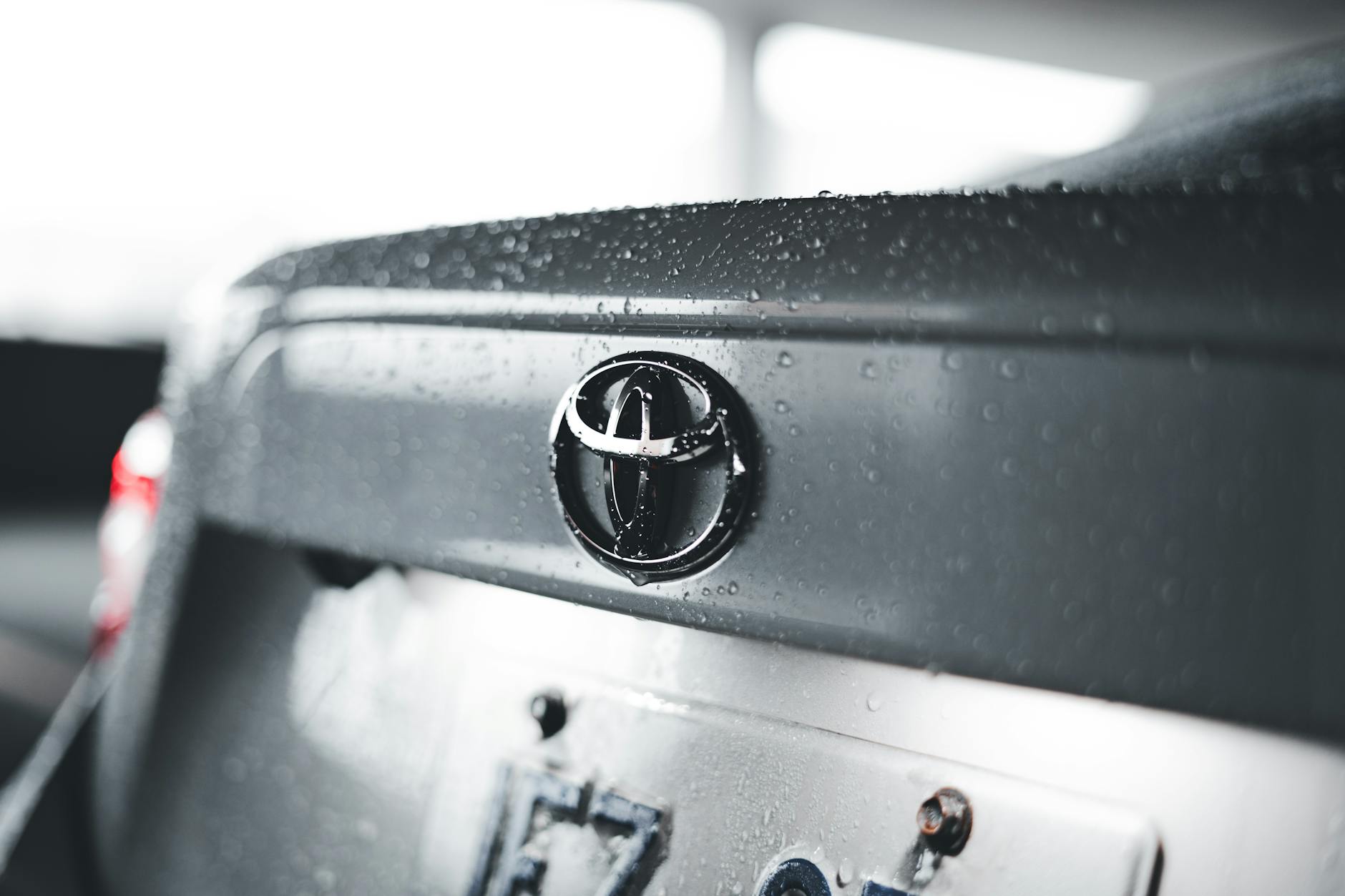 Ilustrasi: Detailed close-up of a raindrop-covered car emblem on a Toyota vehicle.