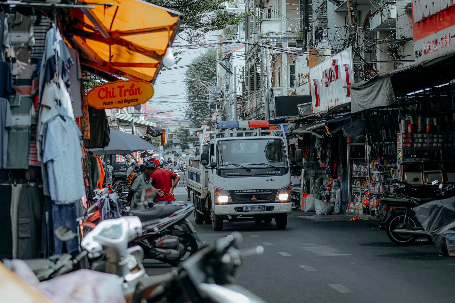 Ilustrasi: Urban street market scene with motorbikes and a Mitsubishi truck, vibrant everyday life.