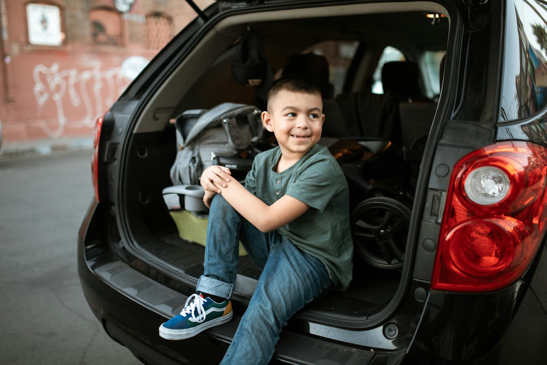 Ilustrasi: Smiling child sitting in the trunk of an SUV on an urban street, wearing casual clothes.