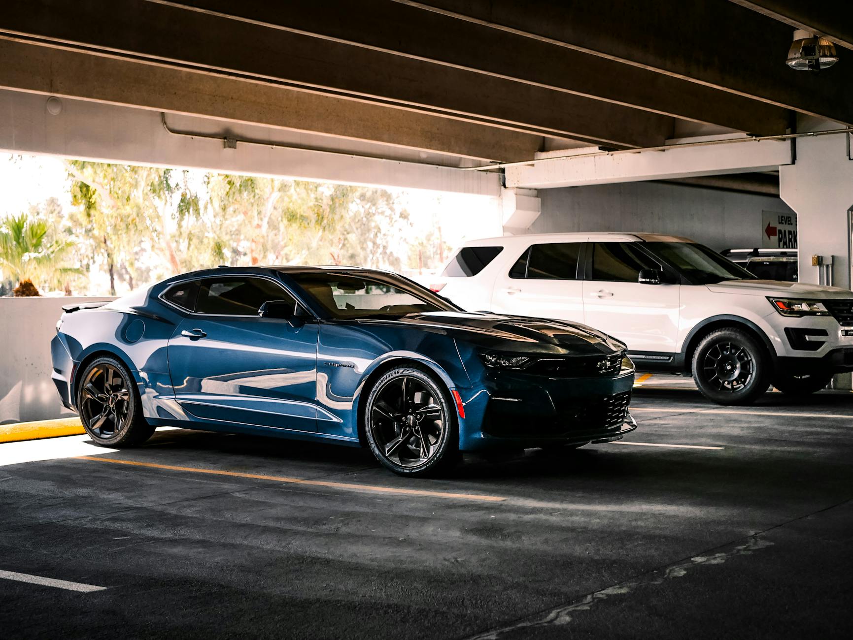 Ilustrasi: Luxurious blue sports car parked indoors beside a white SUV in urban garage setting.