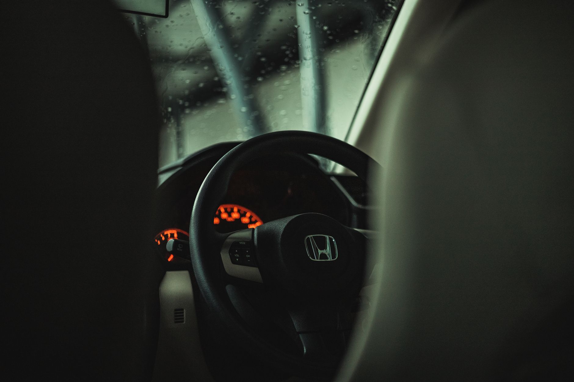 Ilustrasi: Close-up view of an illuminated car dashboard and steering wheel in dim lighting, highlighting the Honda logo.