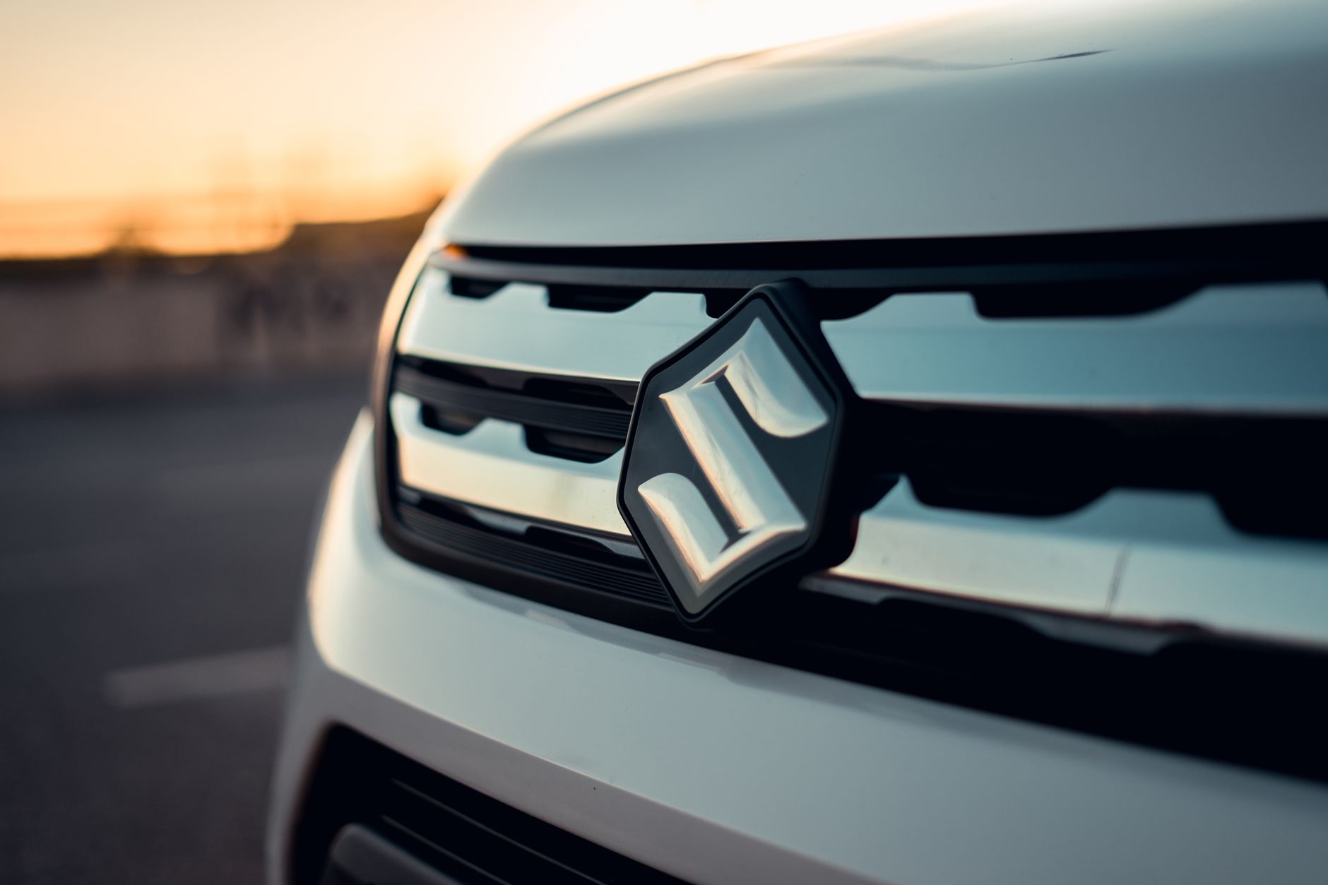 Ilustrasi: Detailed view of Suzuki car grille and logo captured at sunset, showcasing modern automotive design.
