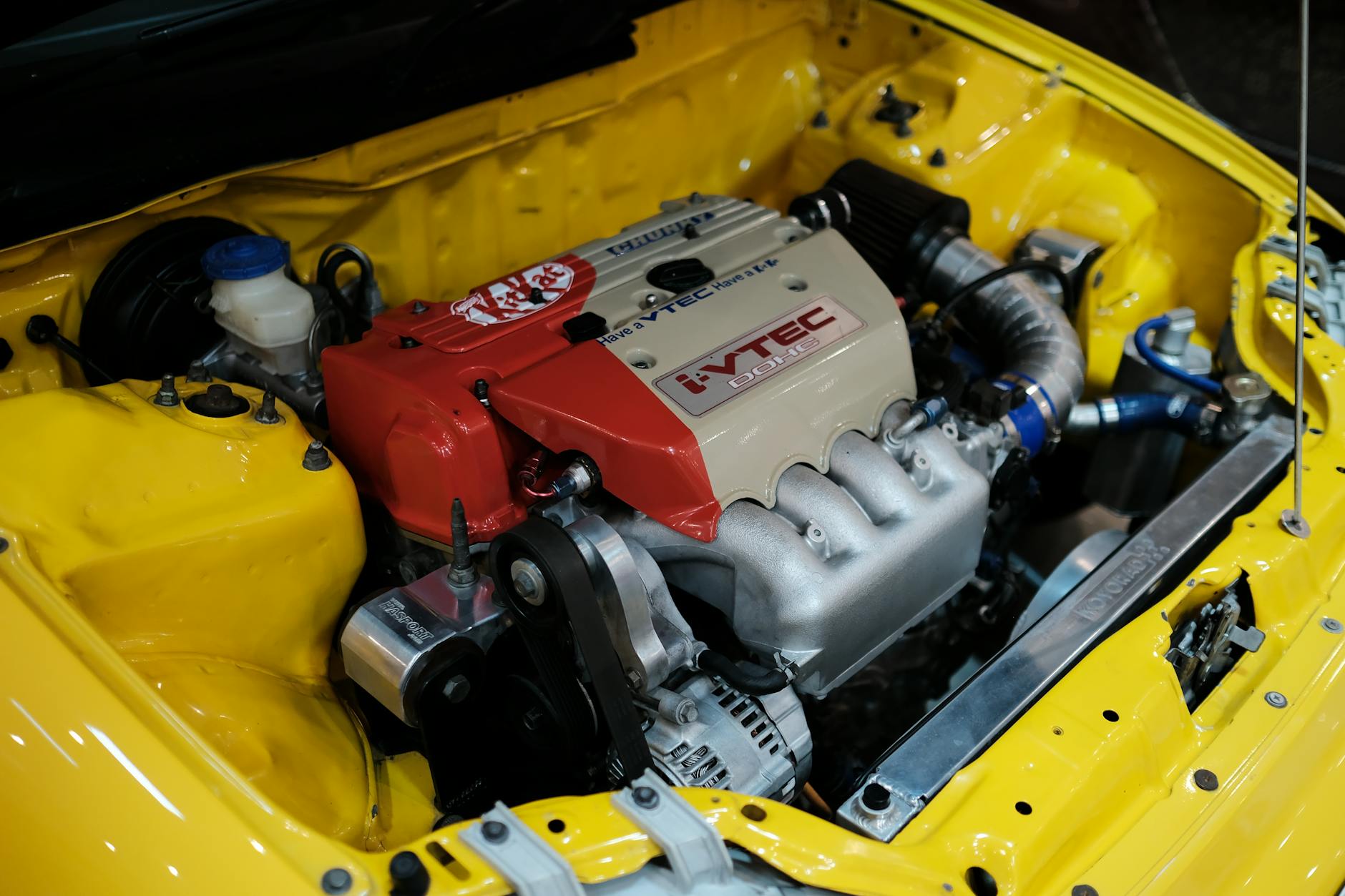 Ilustrasi: Close-up of a high-performance VTEC engine in a yellow Honda, showcasing automotive engineering.