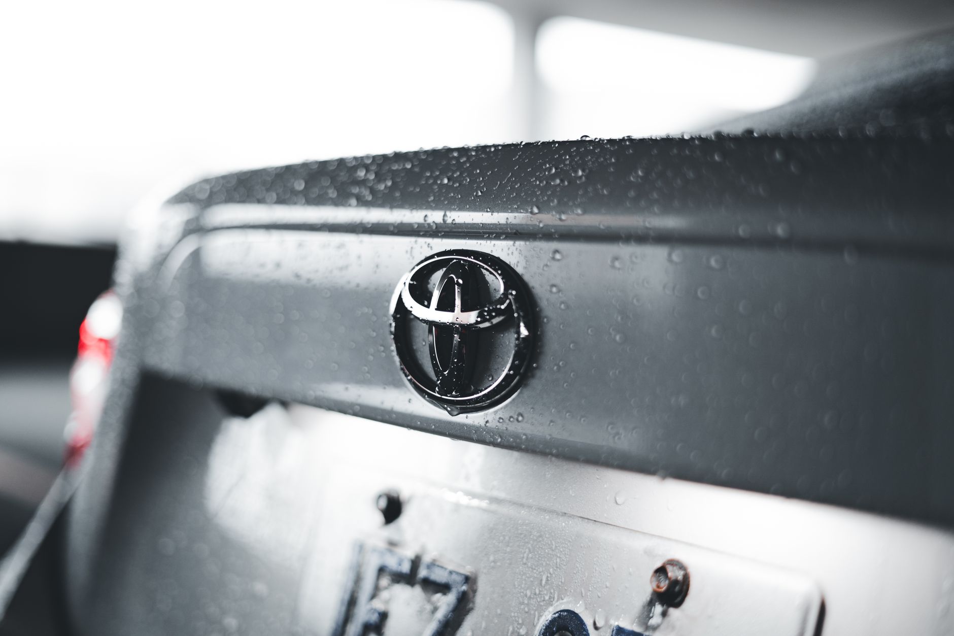 Ilustrasi: Detailed close-up of a raindrop-covered car emblem on a Toyota vehicle.