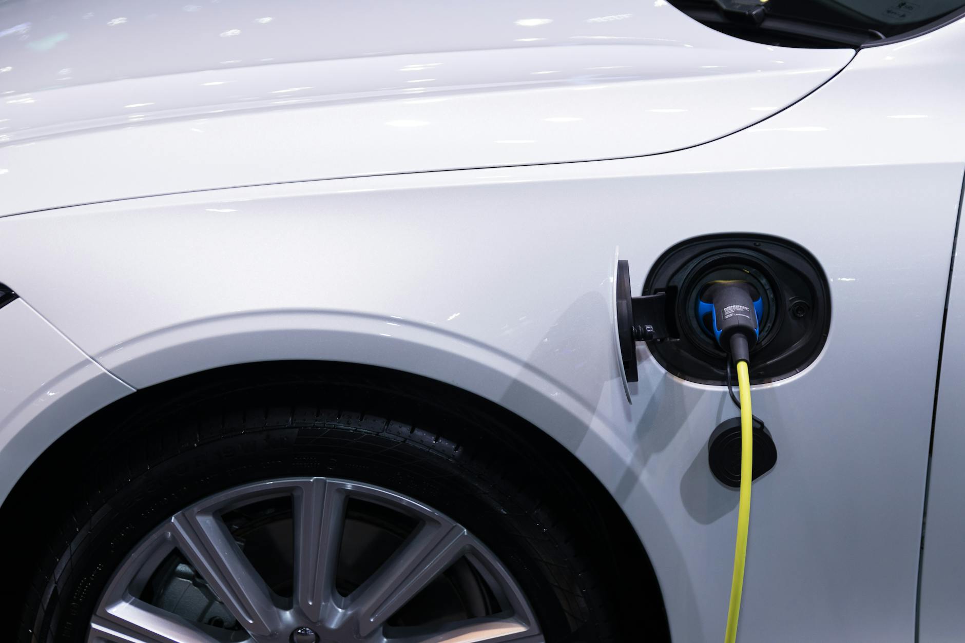 Ilustrasi: A white electric car is plugged in for charging, close-up view of the charging port.