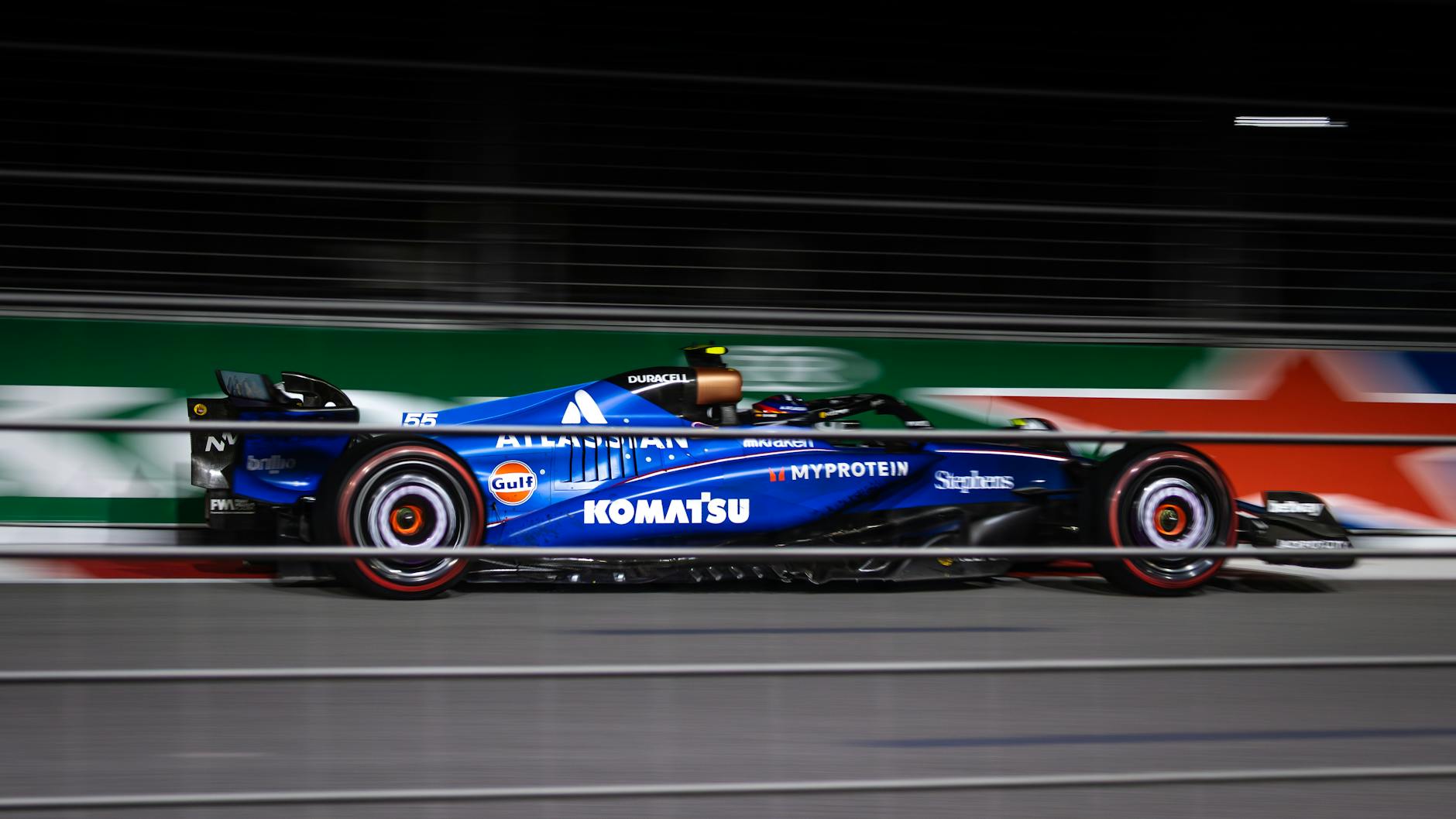 Ilustrasi: Blue Formula car speeding on track during night race.