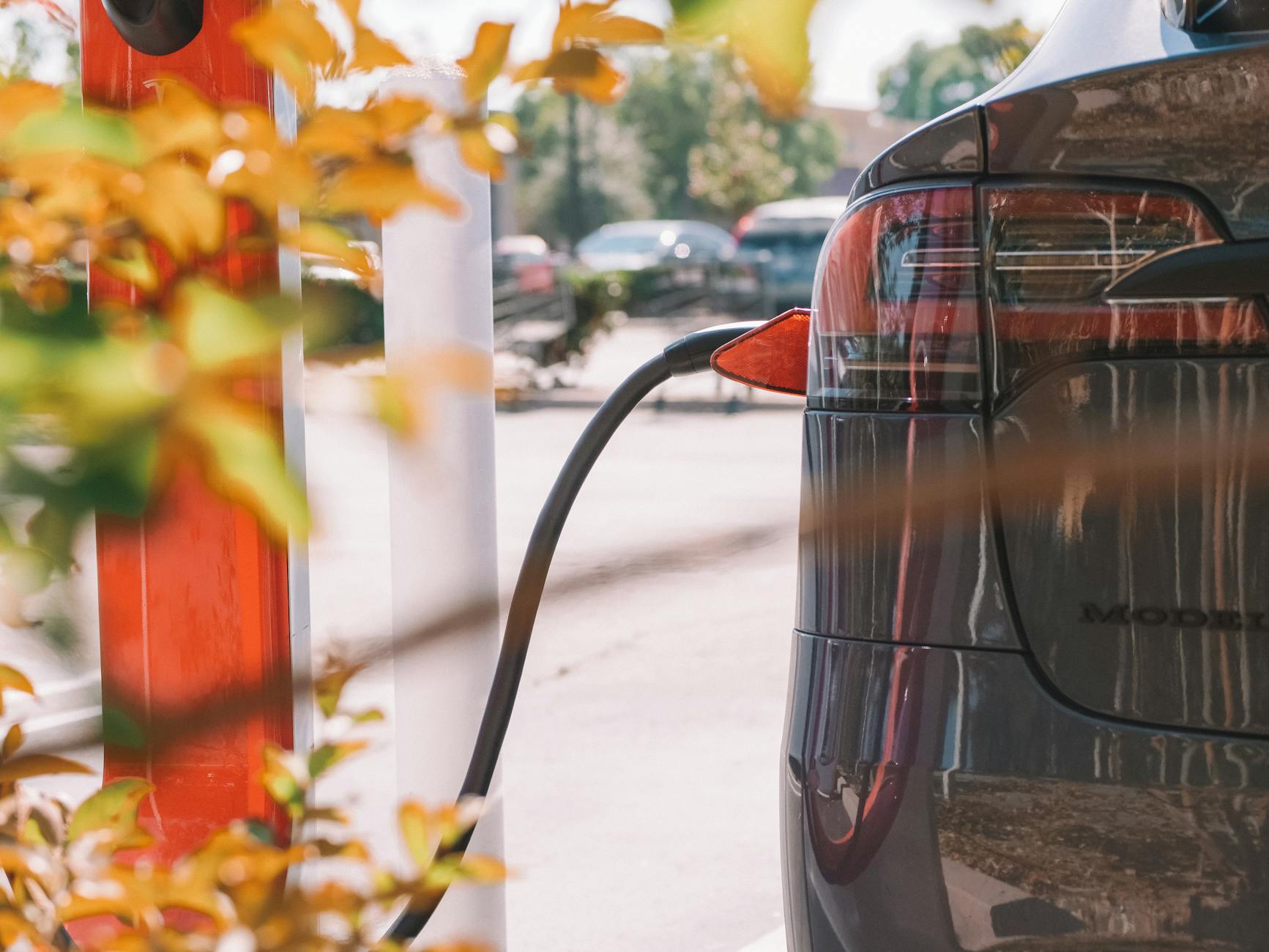 Ilustrasi: Close-up of an electric car charging at a station with blurred cars in the background.