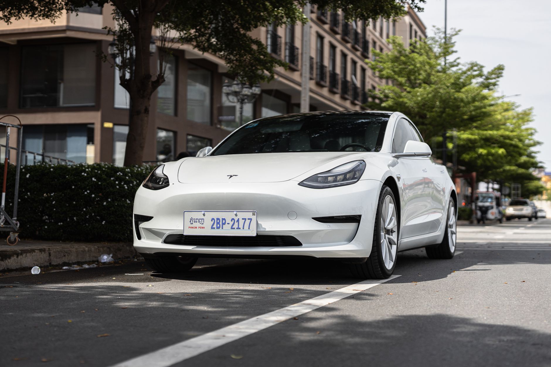 Ilustrasi: A sleek white Tesla Model 3 parked on a city street under trees, showcasing modern automotive design.
