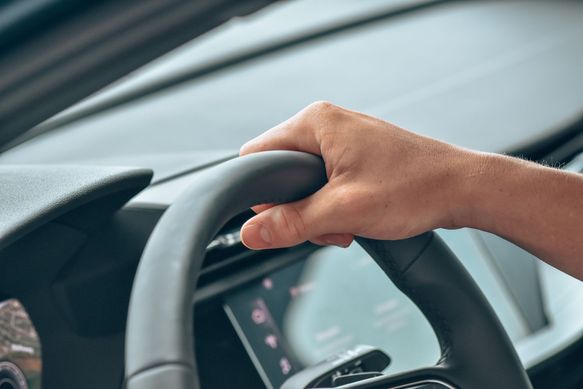 Ilustrasi: A close-up shot of a hand gripping a steering wheel in a modern car interior.