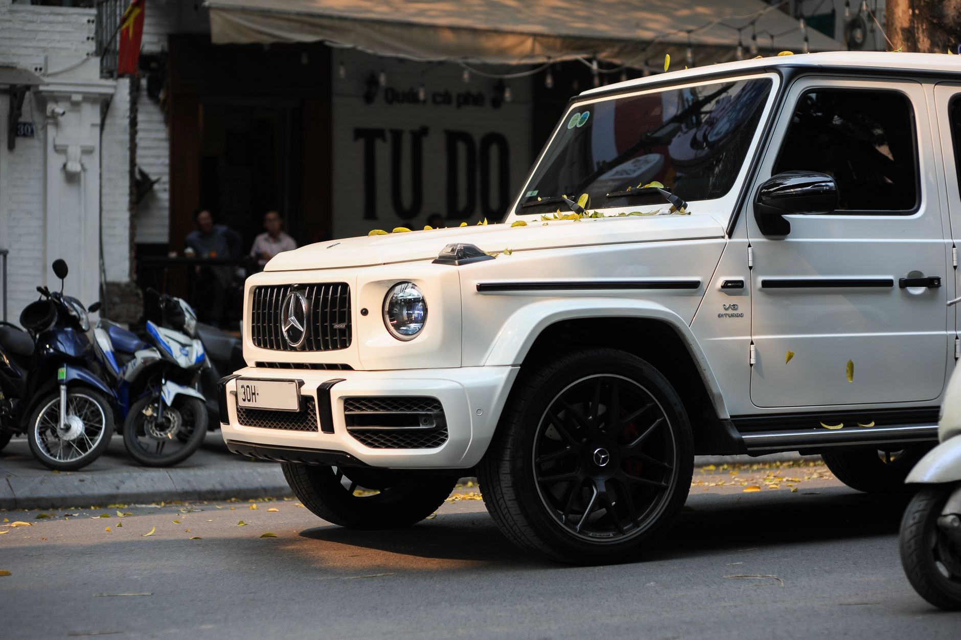 Ilustrasi: A luxury white SUV parked on a bustling city street with motorcycles nearby, capturing urban elegance.