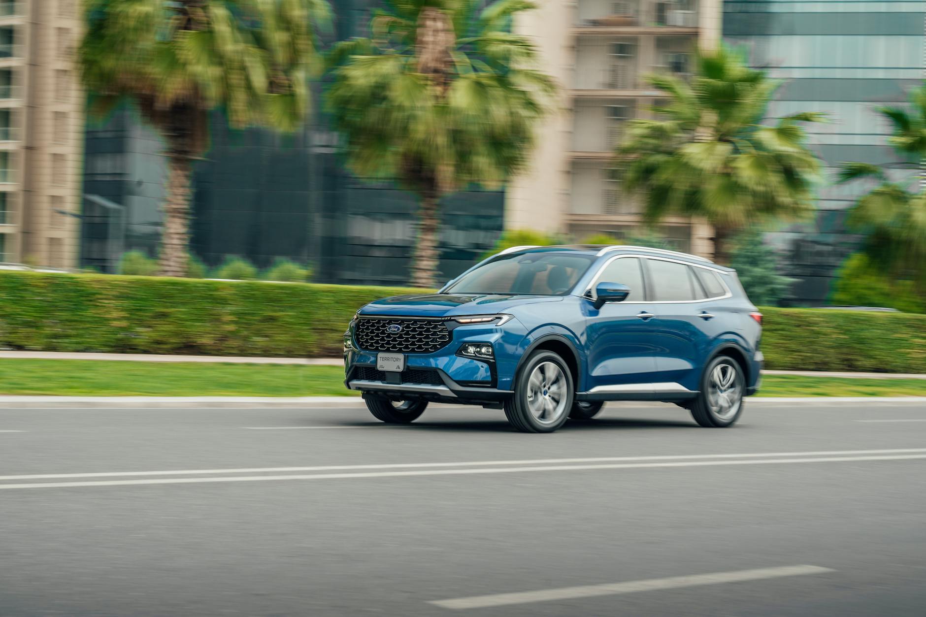 Ilustrasi: Blue SUV driving on a modern street in Erbil, Iraq with palm trees and buildings.