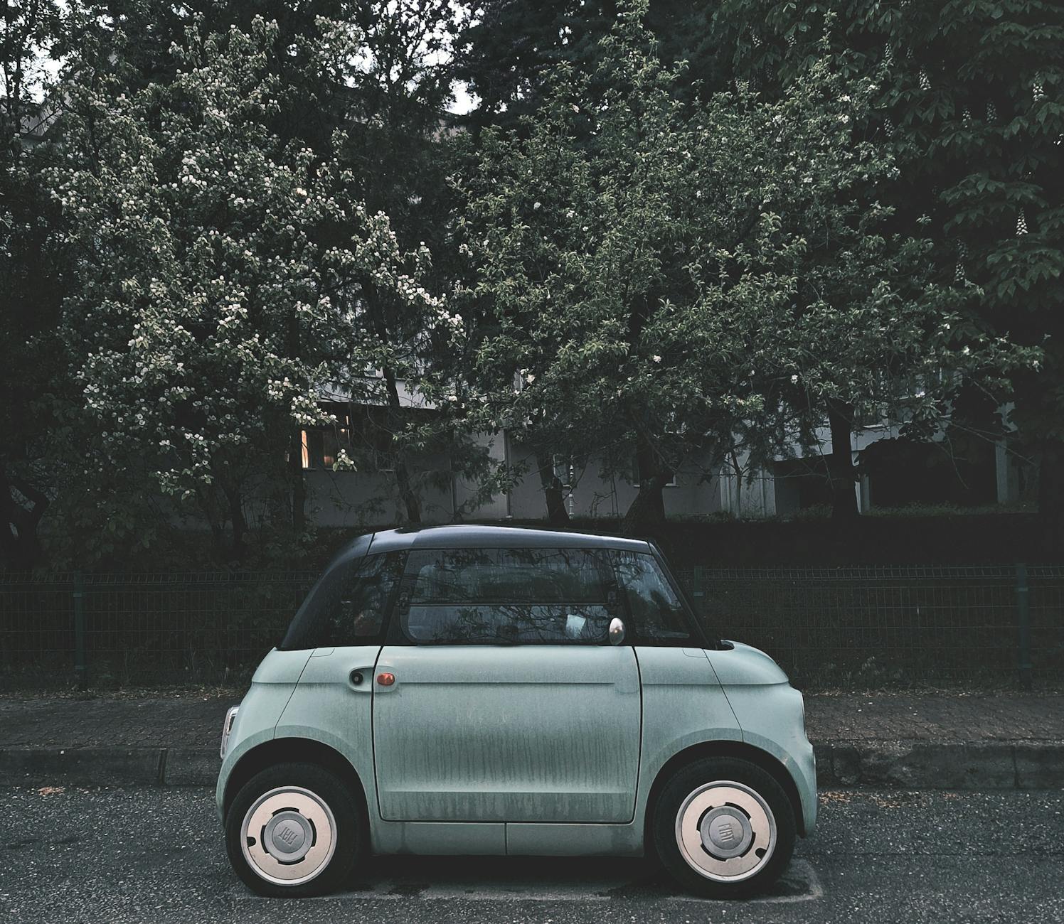 Ilustrasi: A modern compact electric car parked under blooming trees on a city street, highlighting urban eco-friendly transportation.