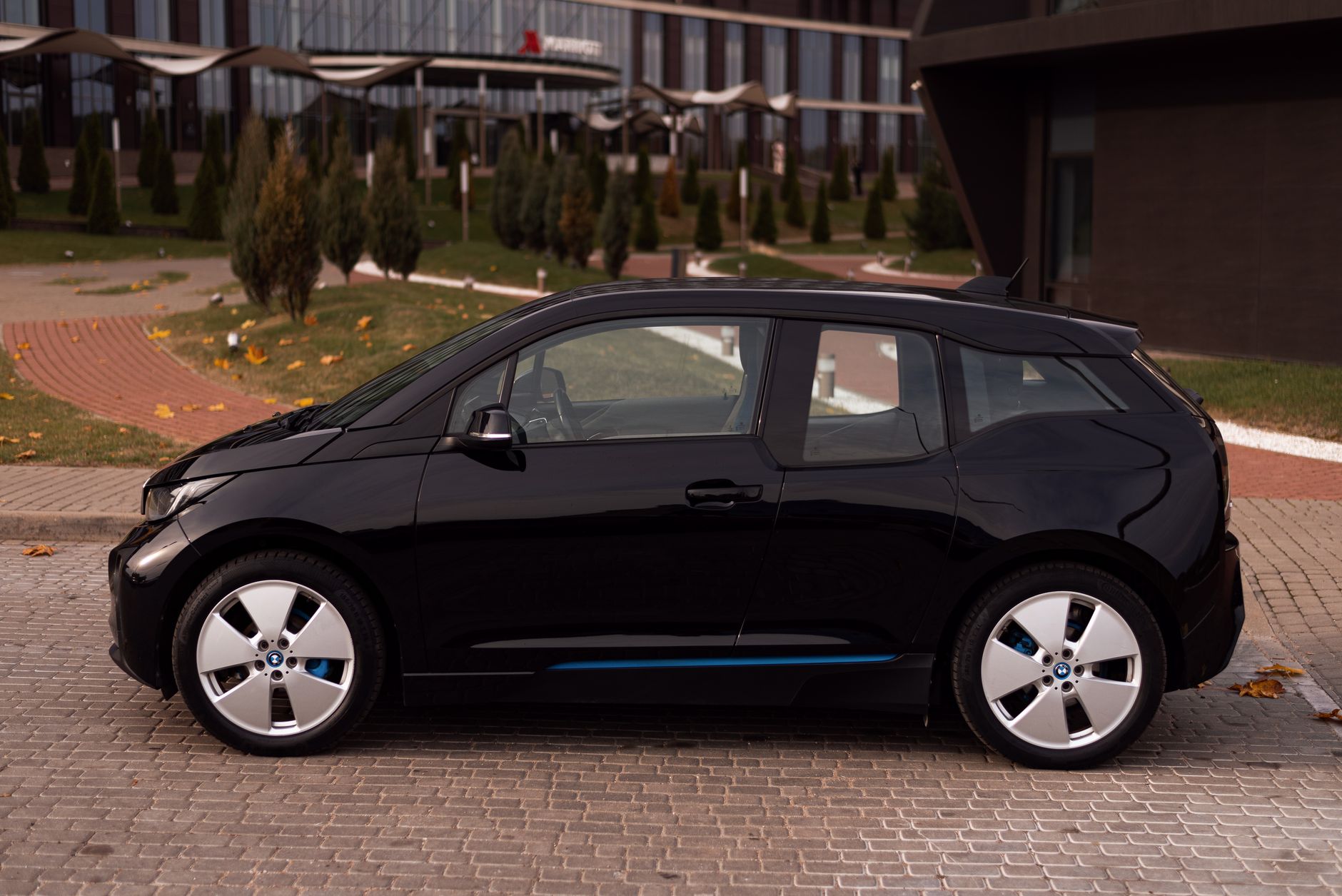 Ilustrasi: Black electric car parked on a city street with modern architecture in the background.