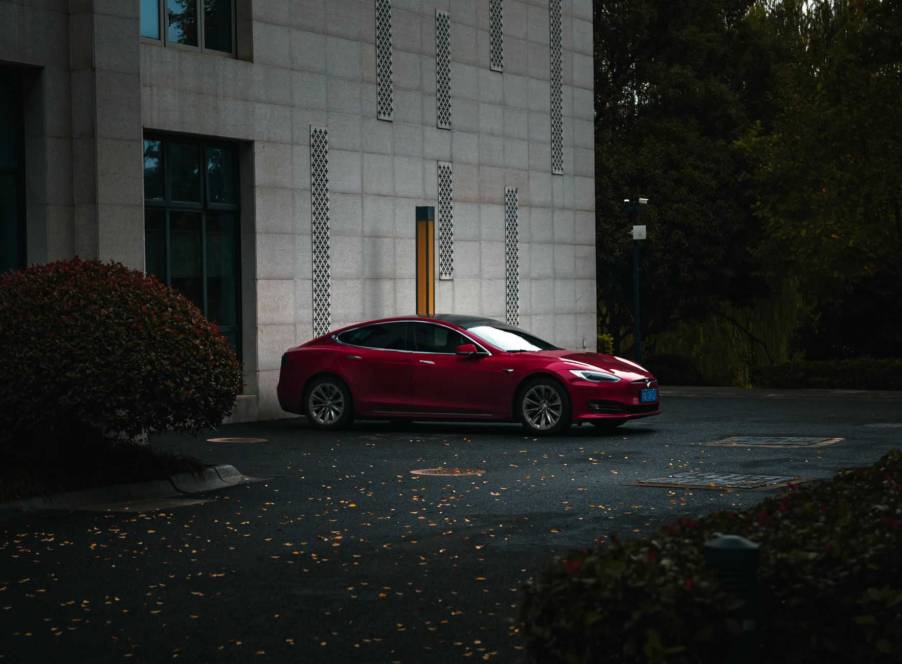 Ilustrasi: A sleek red electric car parked beside a modern building in an urban environment.