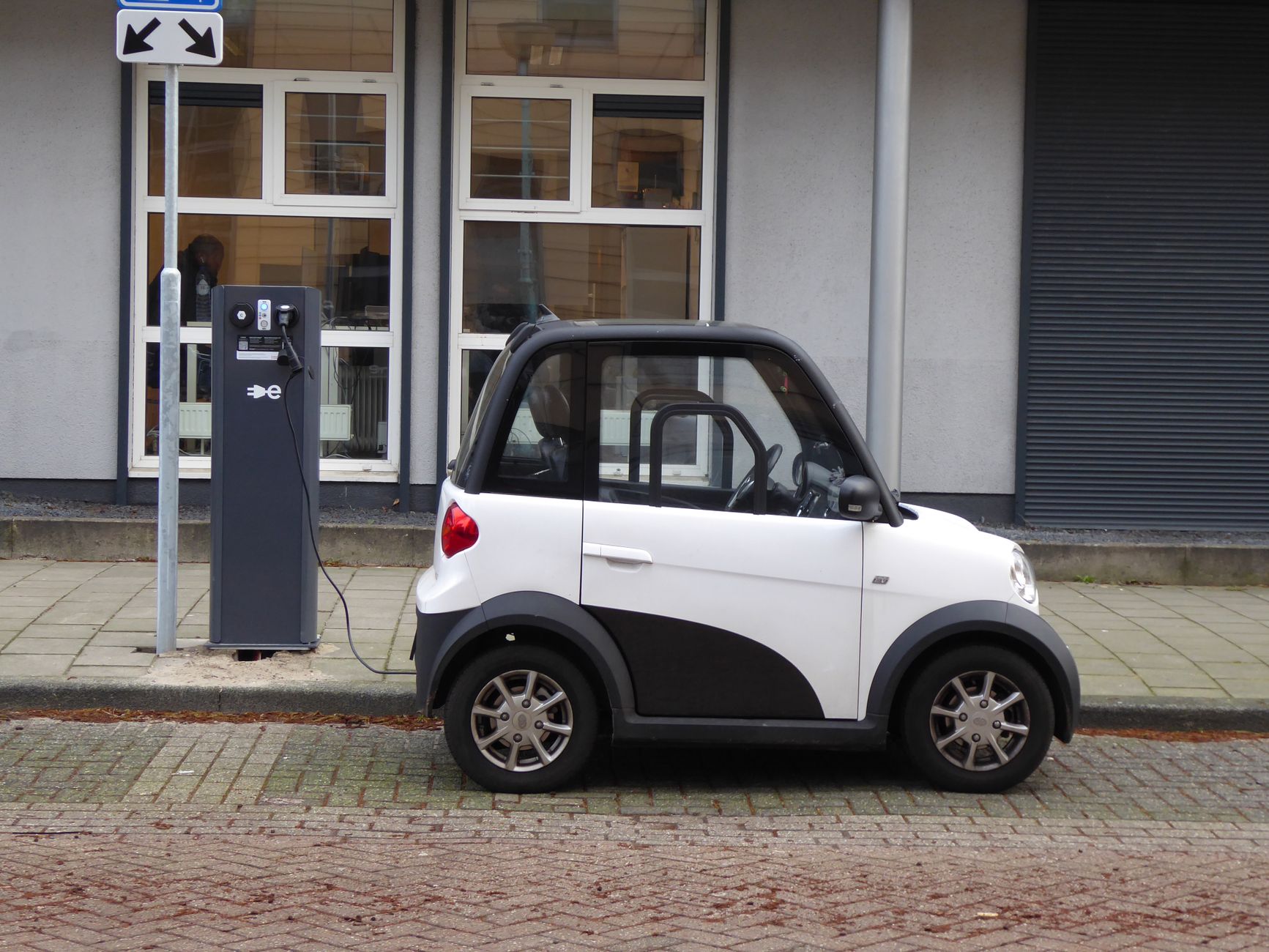 Ilustrasi: A white and black compact electric car charging at a public power station.