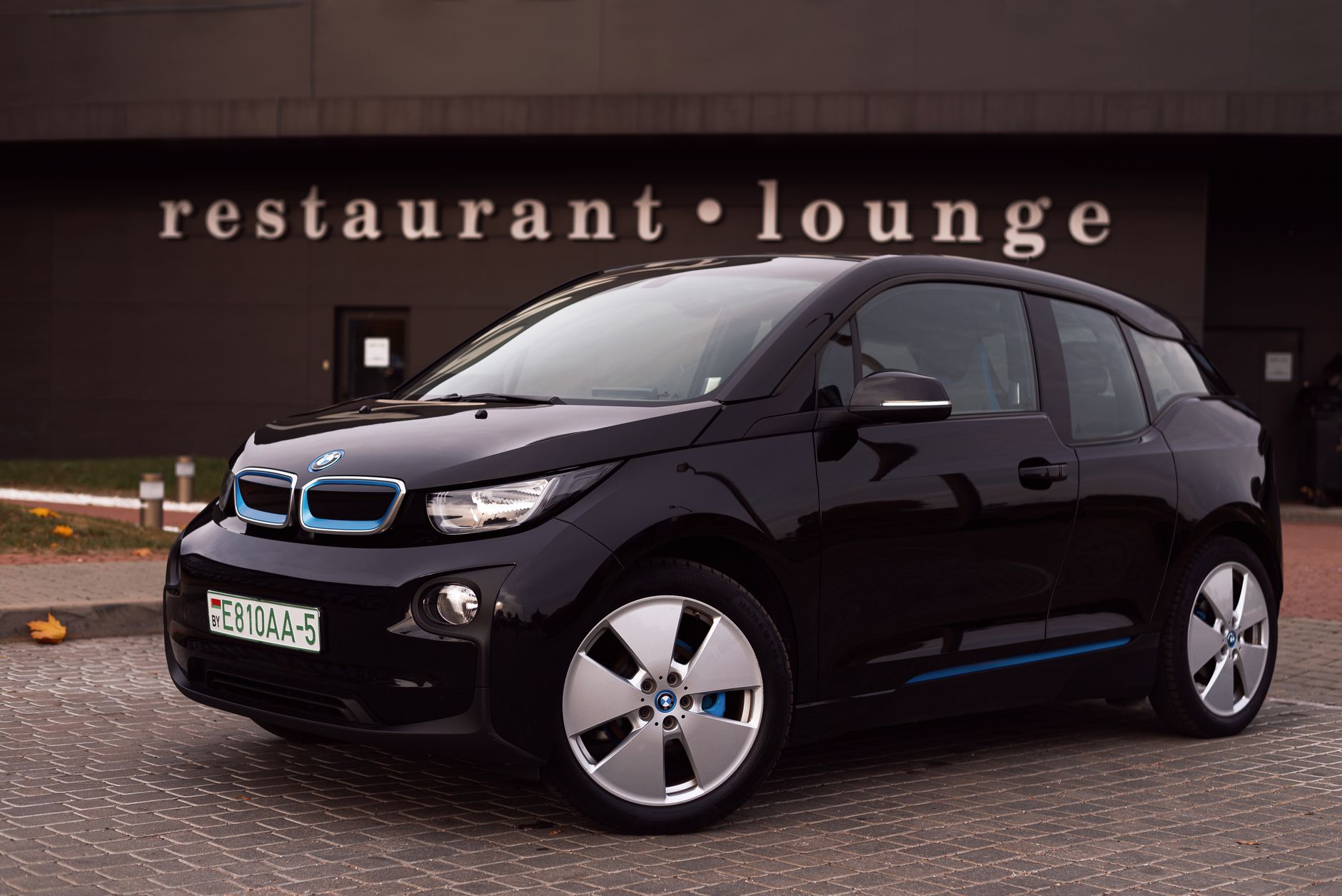 Ilustrasi: Modern black electric vehicle parked outside a stylish restaurant-lounge in the city.