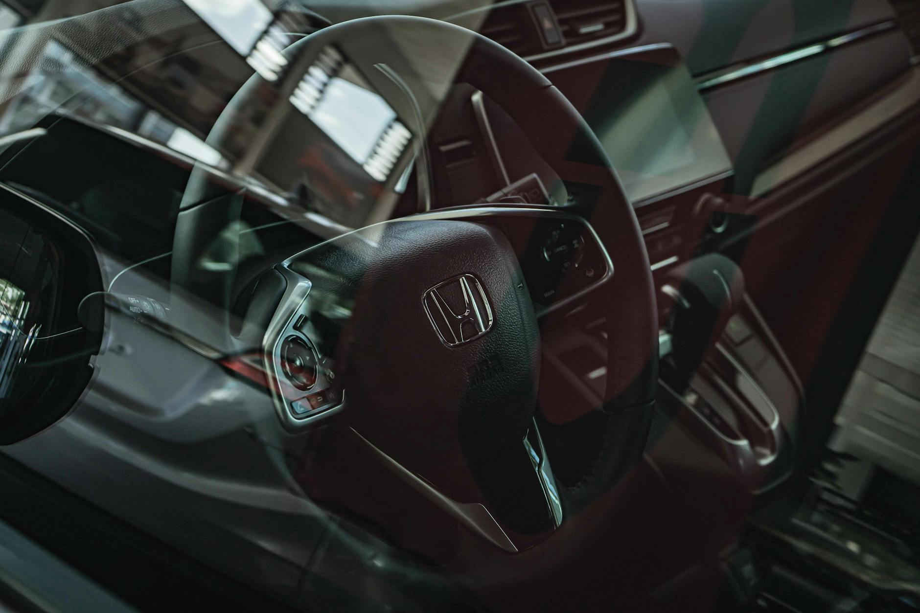 Ilustrasi: Close-up of a Honda car interior highlighting the steering wheel through a reflective glass view.