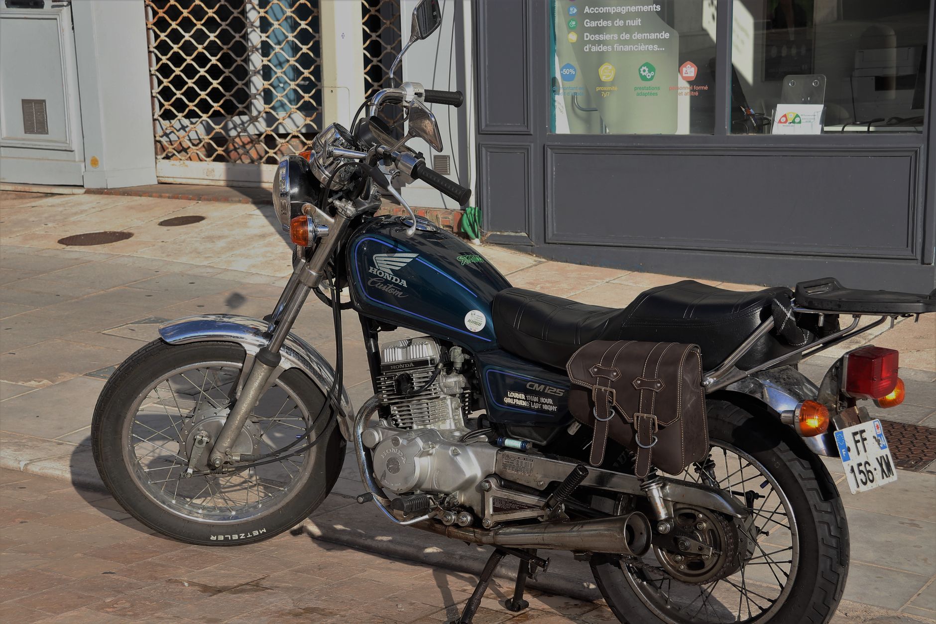 Ilustrasi: Vintage Honda CM 125 motorcycle parked on a sunny street with a side saddlebag.