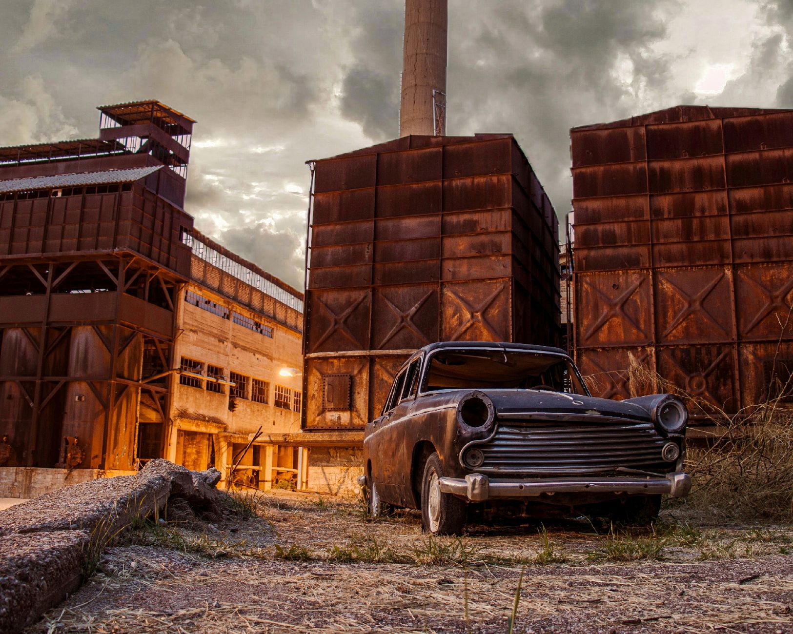 Ilustrasi: A scene of decay with a rusty car parked in front of an old industrial factory.