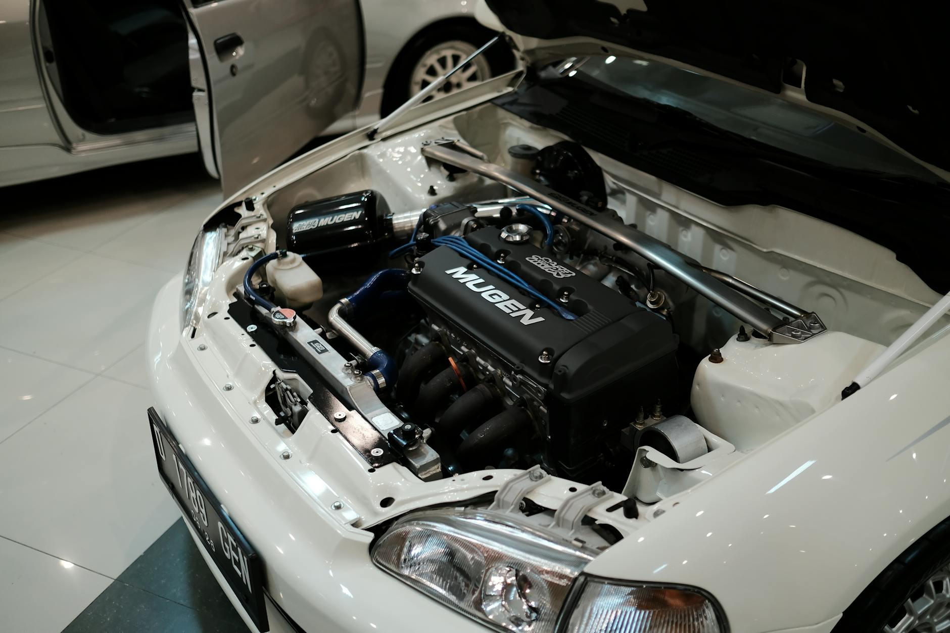 Ilustrasi: Detailed close-up of a Mugen-tuned Honda engine in a white car, showcasing automotive performance.